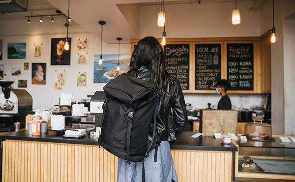 Woman in a coffee shop looking at the menu while wearing the Shadow Guide 33 over one shoulder.